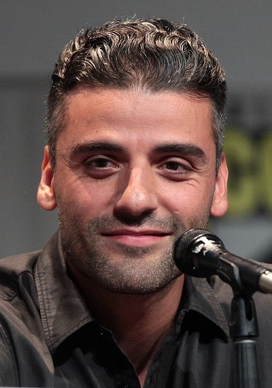 Diese Fotografie zeigt das Portrait des amerikanischen Schauspielers Oscar Isaac im Jahr 2015 auf der San Diego Comic Con. Er schaut freundlich in die Kamera, vor ihm ist ein Mikrofon aufgestellt.