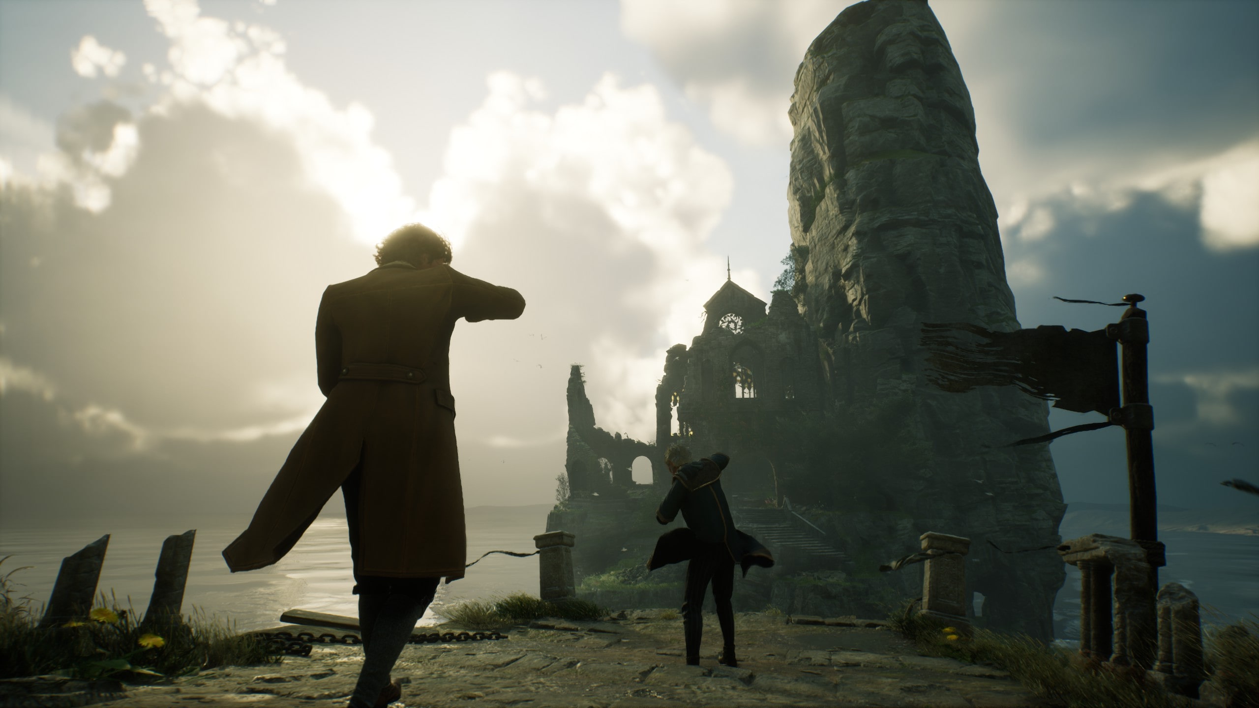 Dargestellt ist ein Screenshot aus Hogwarts Legacy. Zu sehen ist Klippe am Meer. In einen mächtigen Felsen ist eine zerstörtes Gebäude eingelassen. Zwei Zauberer laufen darauf zu. Der Wind scheint stark zu sein, da die Charaktere ihre Arme schützend vor das Gesicht halten. 