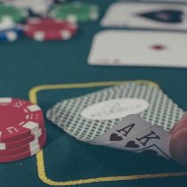Zu sehen ist ein Blackjack-Tisch auf dem einige Karten und Spielchips liegen. Eine Hand deckt spitzen Fingern zwei Karten auf.
