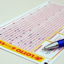 Zu sehen ist ein Standard 6 aus 49 Lottoschein uaf einem Tisch. Auf dem Schein liegt ein Kugelschreiber.
