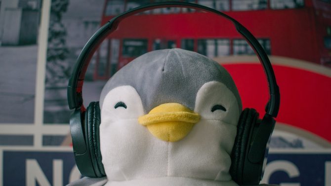Zu sehen ist ein Pinguin Kuscheltier, welches Kopfhörer trägt und glücklich schaut.
